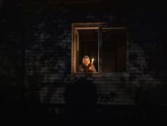 70-летняя Екатерина смотрит в окно, держа свечу в своем доме во время отключения электроэнергии, Бородянка, Киевская область, Украина, четверг, 20 октября 2022 года. Фото: Francisco Seco / AP
