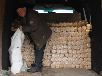 Житель Бахмута собирает хлеб для соседей по бомбоубежищу в пункте раздачи гуманитарной помощи. Фото: Clodagh Kilcoyne / Reuters